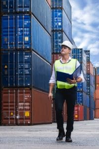 Man in hard hat walking around a shipping container yard