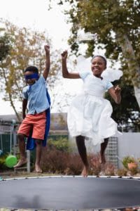 Two African American siblings having fun jumping on a trampoline