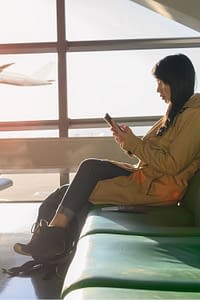 Female waiting in the airport with airplane departing in the background.