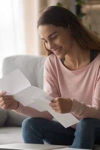 Young woman sitting on sofa reading health reimbursement arrangement letter.