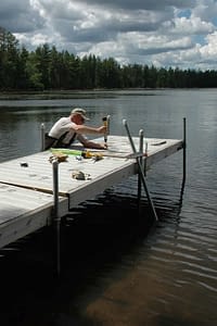 Man wearing waders repairing pier in a lake.