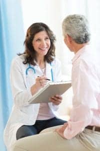 Female Doctor Takes Notes and Smiles at Her Middle-Aged Male Patient