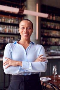 Restaurant owner standing proudly in front of tables and bar.