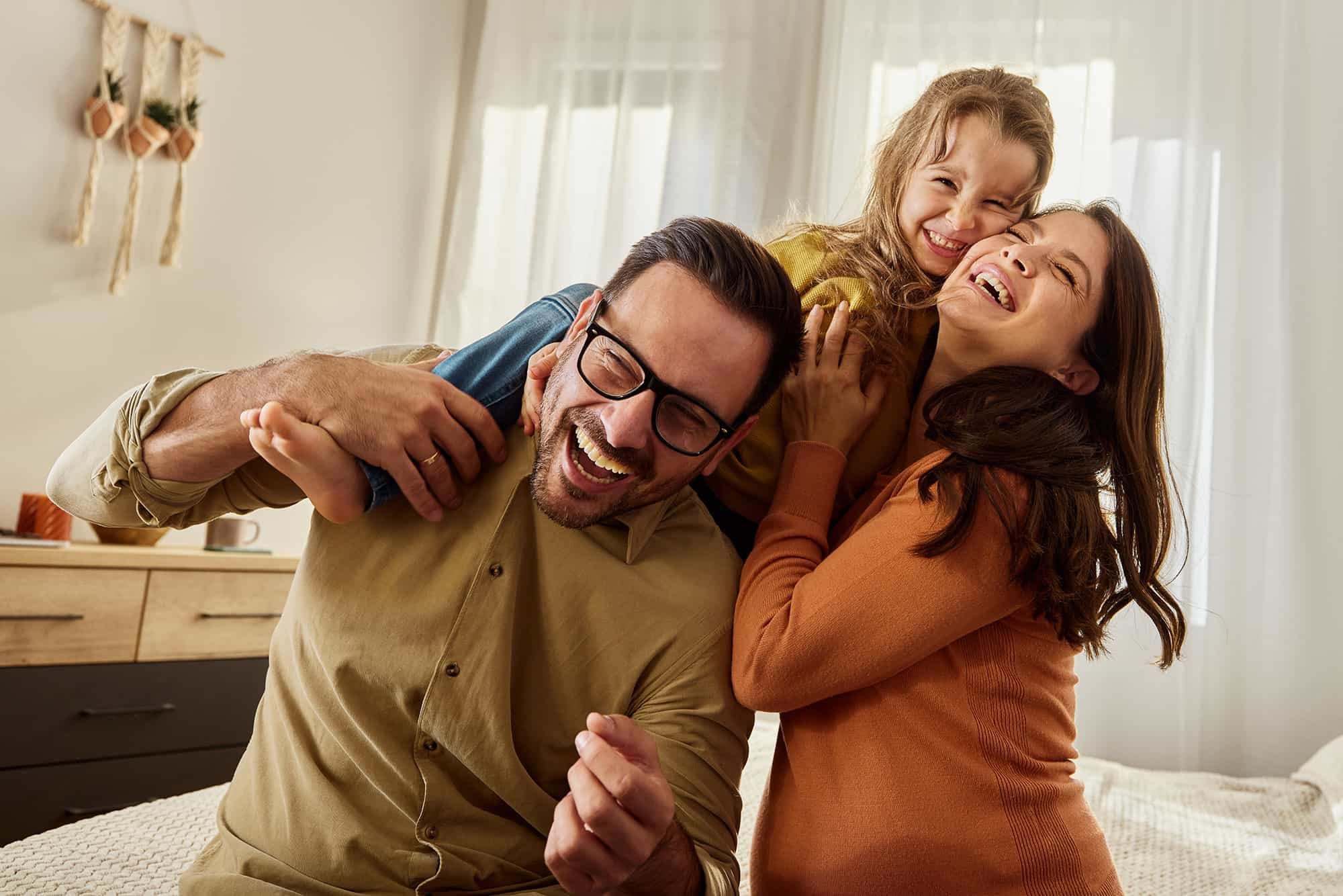 Cheerful girl having fun with her parents in bedroom. Copy space.
