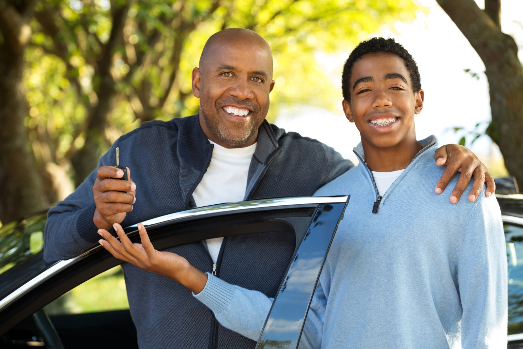 Teenager learning to drive Father and son in front of car holding key.
