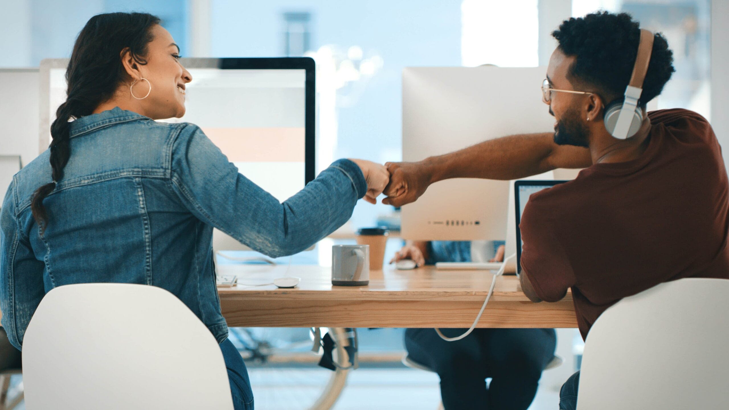 male and female co-workers doing a fist bump at their desks