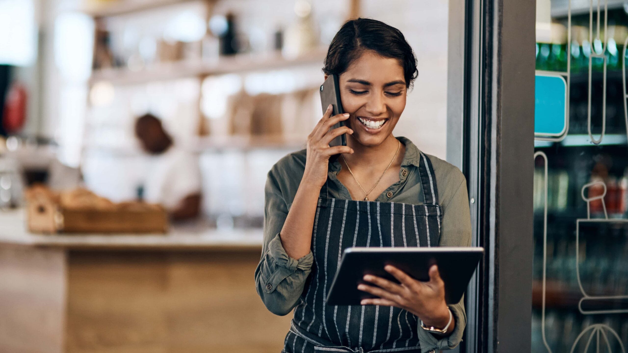 female owner of shop reading on iPad and talking on the phone while smiling