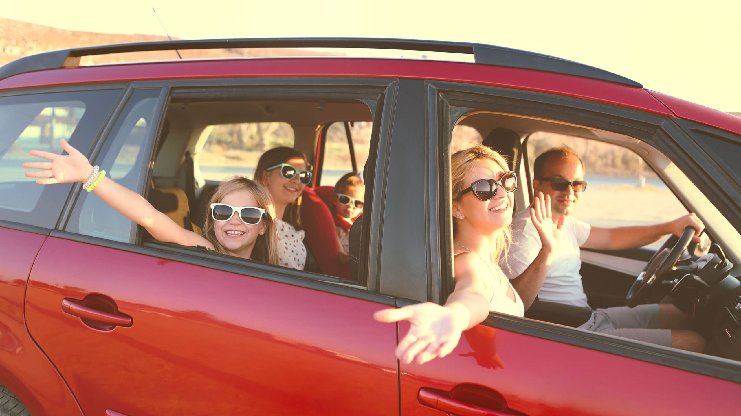Family riding in a red car waving out the windows.