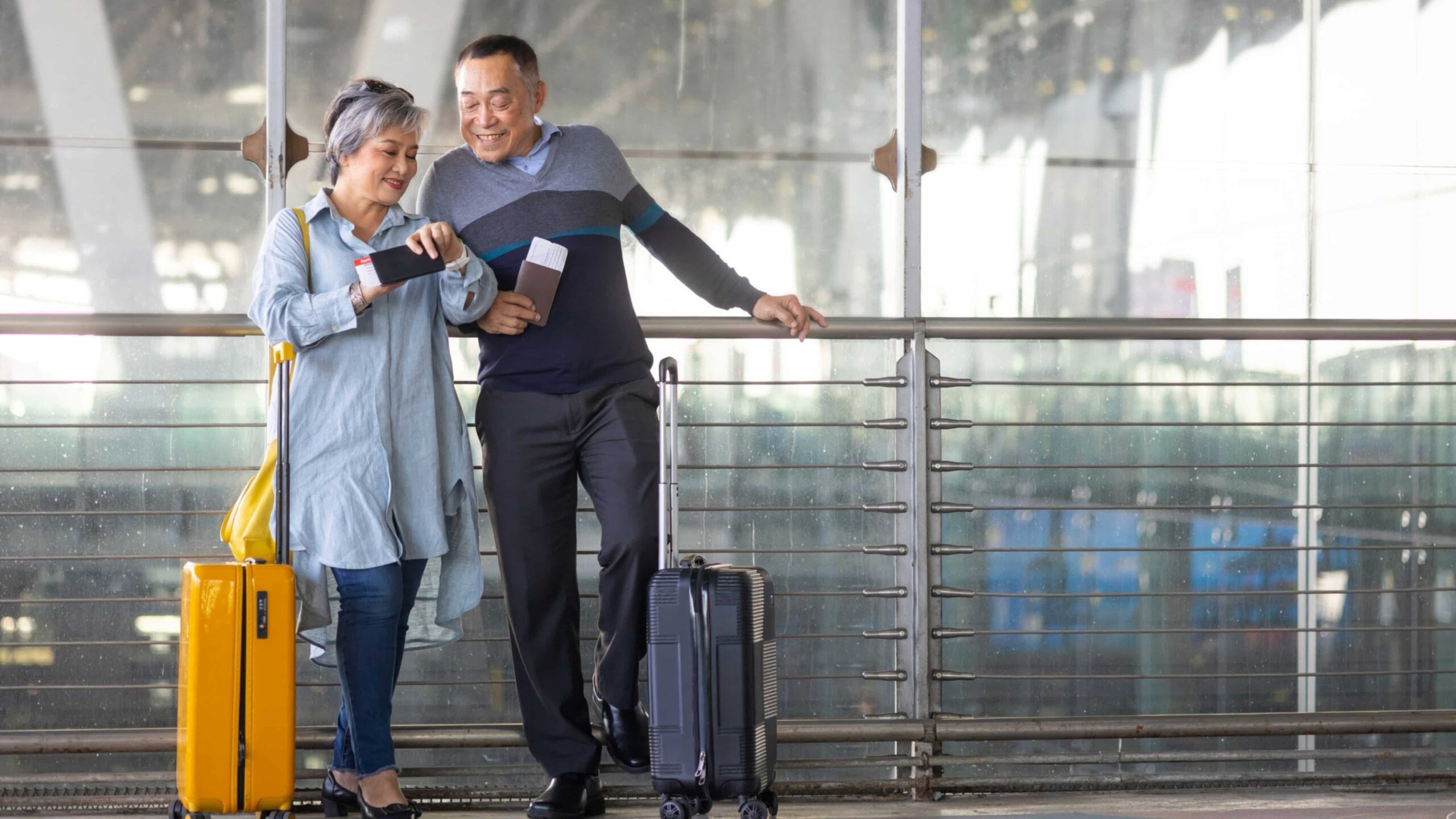 senior asian couple standing with luggage looking at phone