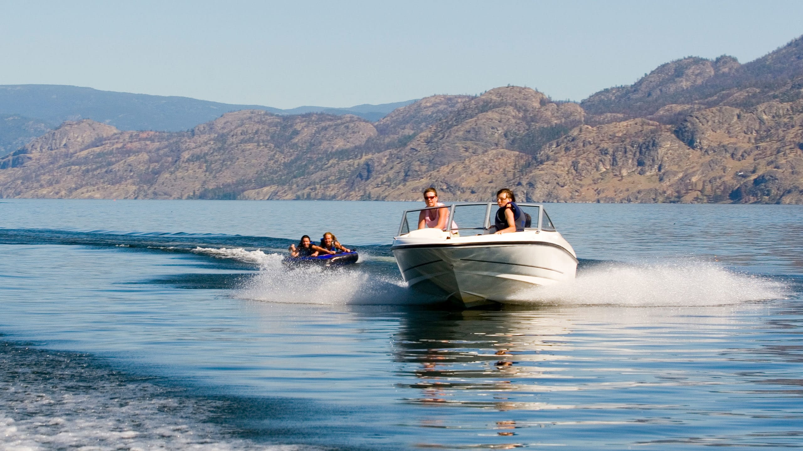 Boat on a lake pulling two people on an inflatable tube.