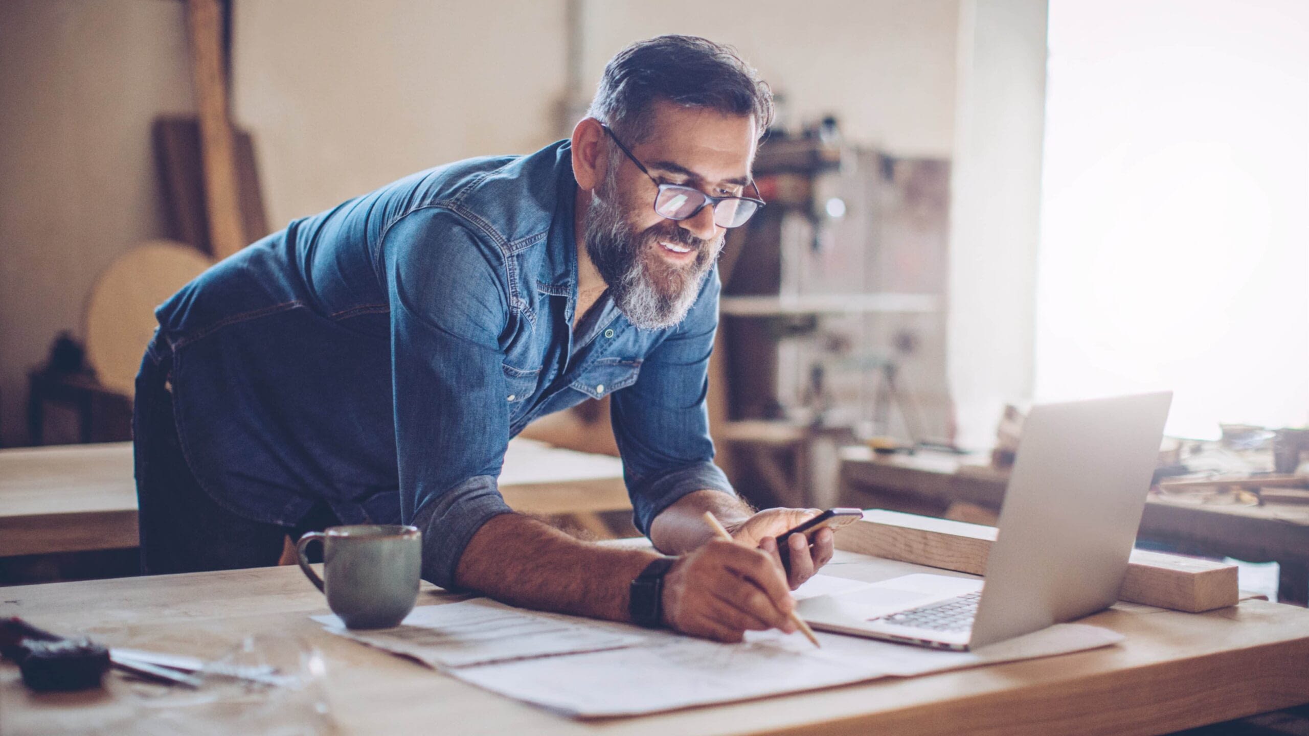 male business owner at desk writing and looking at phone