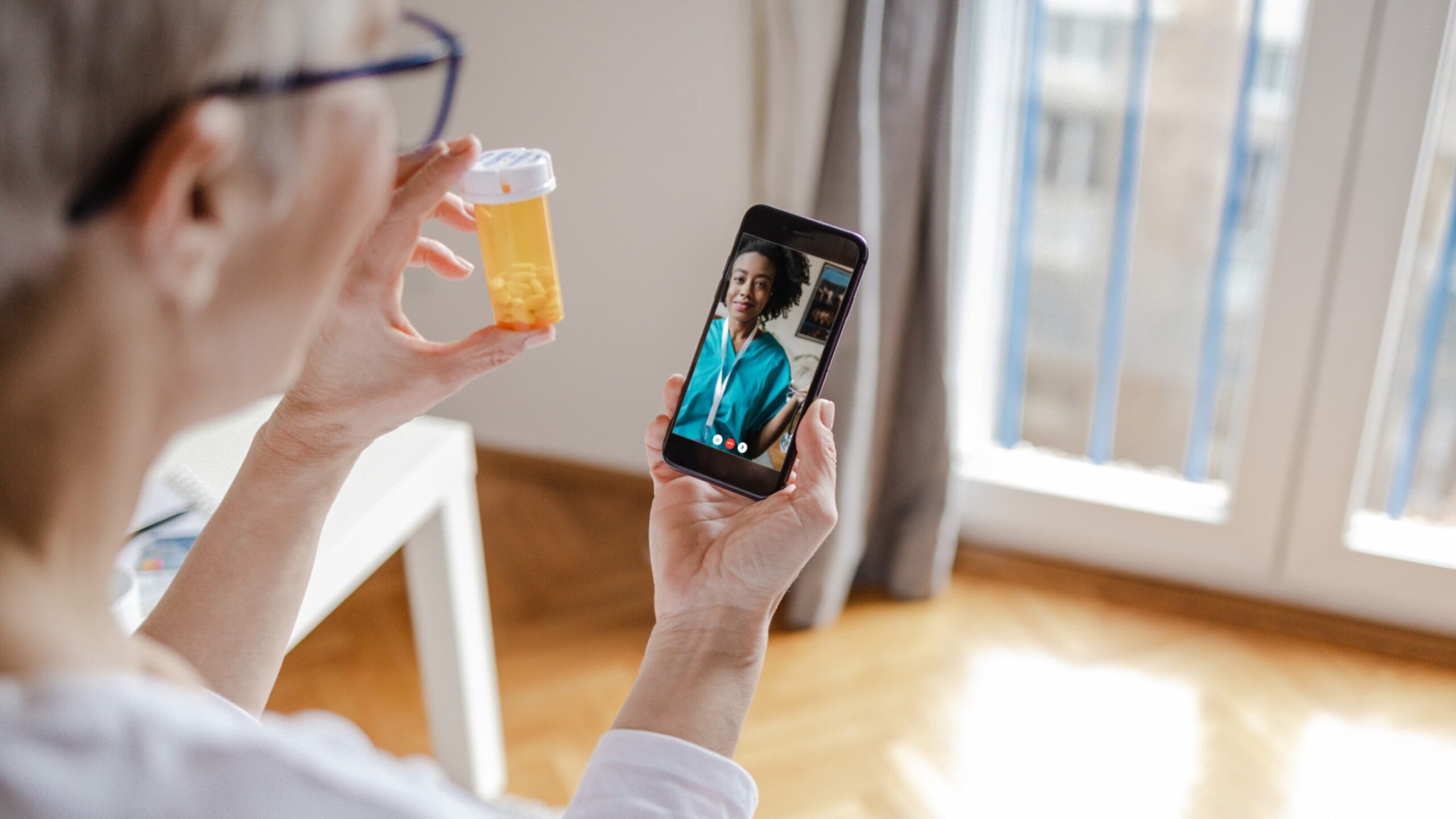 senior woman holding up medication bottle while on a telehealth call with her doctor