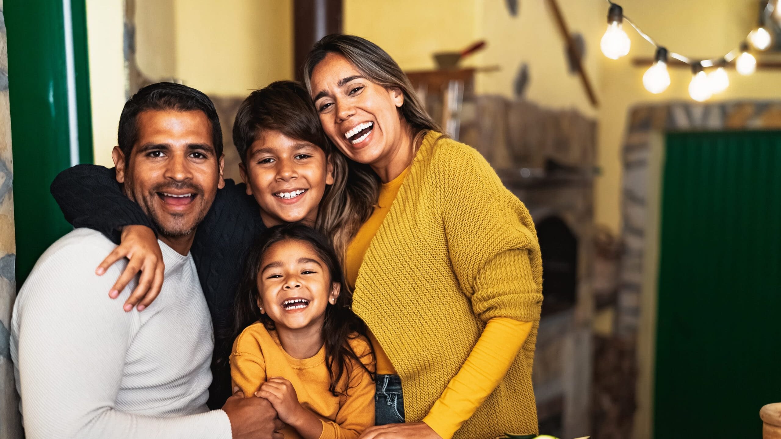 Family of four hugging and smiling for the camera in their kitchen.