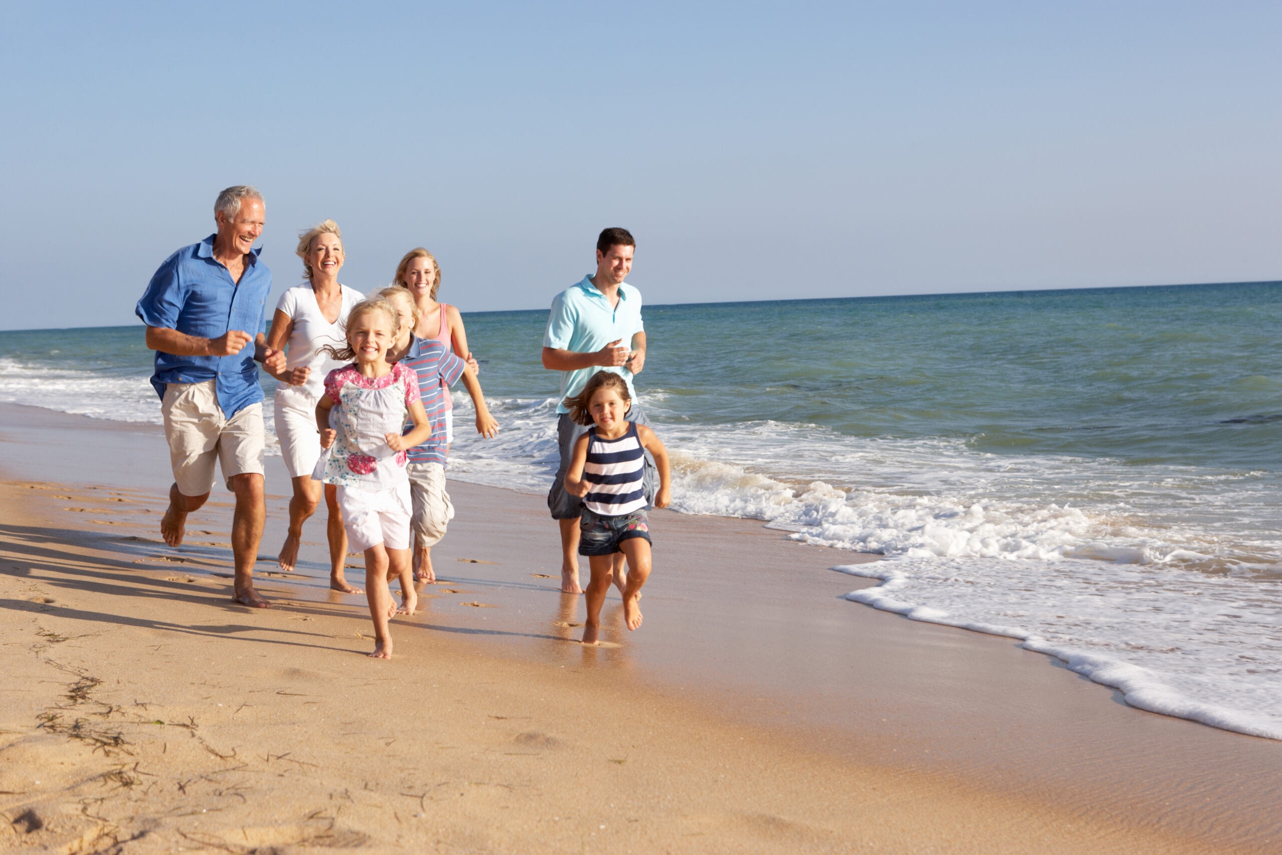 Portrait Of Three Generation Family Running On Beach Holiday