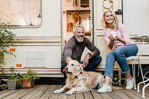 couple sitting outside a travel trailer with their golden retriever