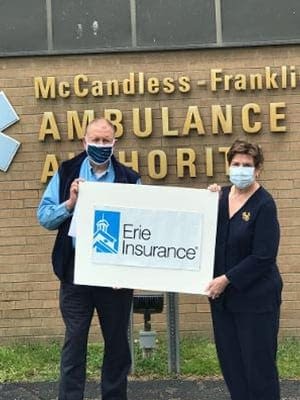 We Don’t Just Sell Policies. We Give Back. Agents Holding Erie Insurance Sign by McCandless-Franklin Park Ambulance Authority