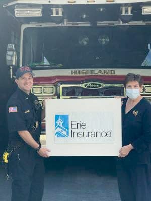 We Don’t Just Sell Policies. We Give Back. Insurance Agents Holding Erie Insurance Sign In Front Of Fire Truck