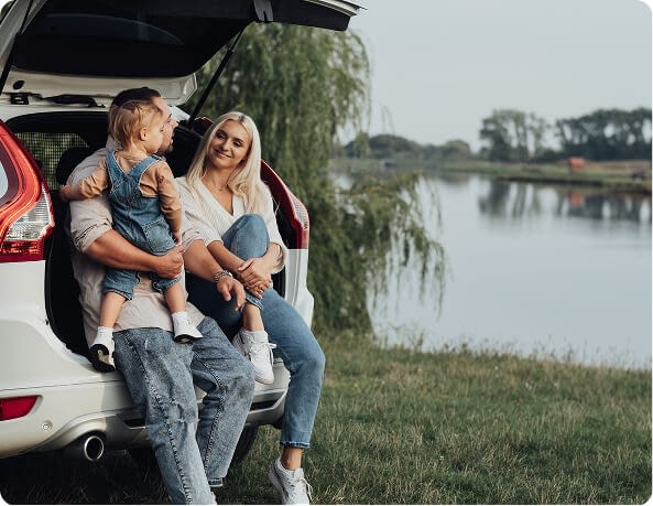 parents with little daughter sitting in open trunk of car