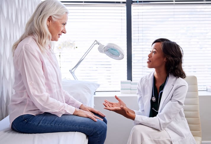 Mature Woman In Consultation With Female Doctor Sitting On Examination Couch In Office Woman In Consultation With Female Doctor