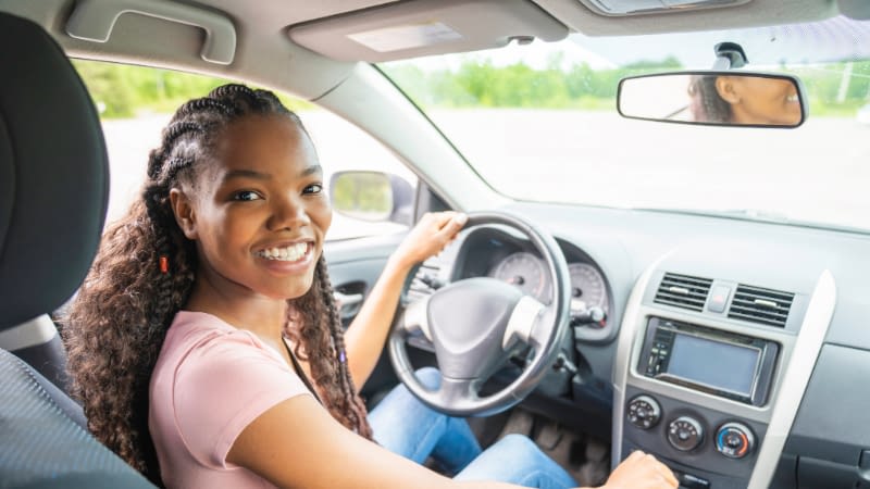 Auto Insurance 61626 Female teen driver sitting in drivers seat looking back smiling