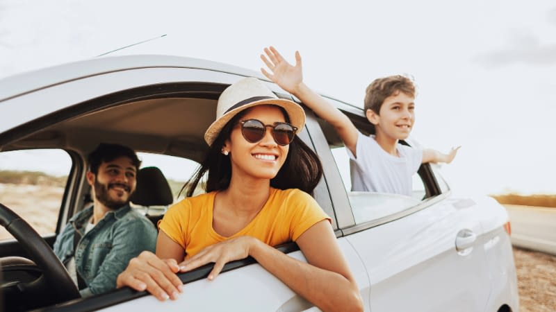 Auto Insurance 6326 Family enjoying road trip. Mom driving and son hanging outthe back window with dad in the passenger seat