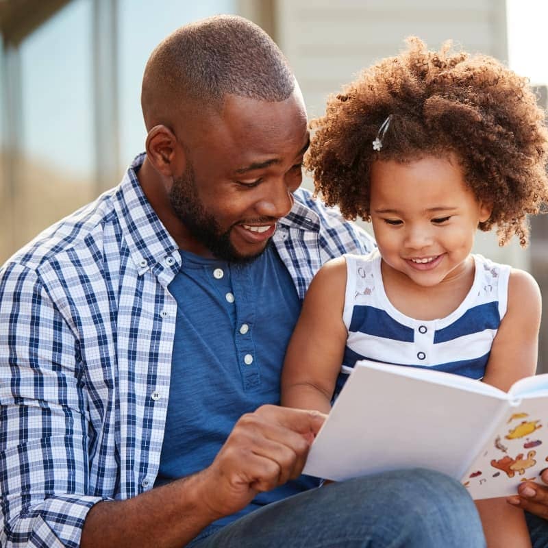 Father and daughter reading a book outside their home