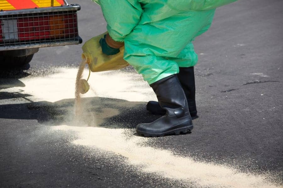 man in hazmat suit pouring a powdered chemical neutralizing agent on the ground