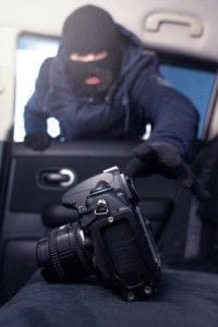 Male robber in black mask stealing forgotten photo camera from car back seat