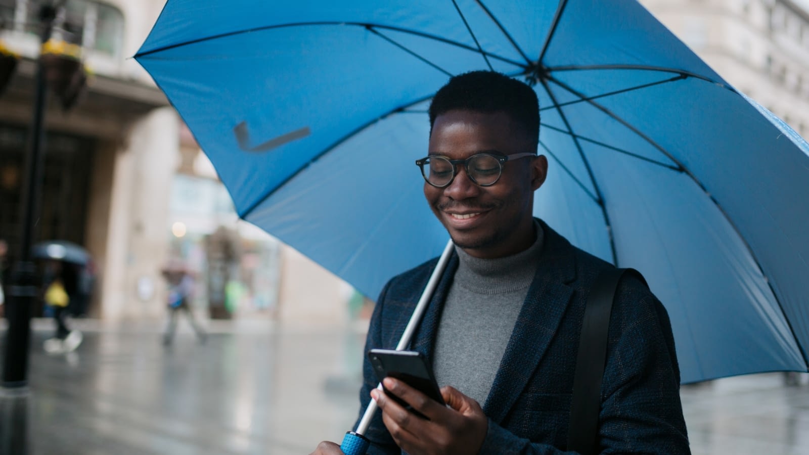 young man holding an umbrella in the rain while looking at his phone