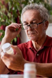 Senior man sitting at table reading the label on a prescription.