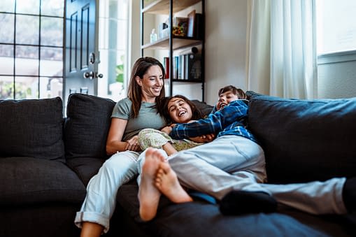 a mother laying up on the couch with her daughter and son right next to her.