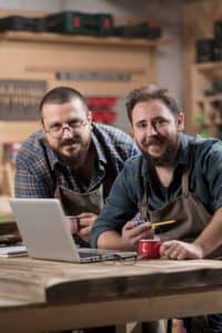 Employer and employee in wood shop looking at laptop.