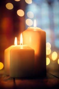 Close up of lit candles with large church windows in the background.